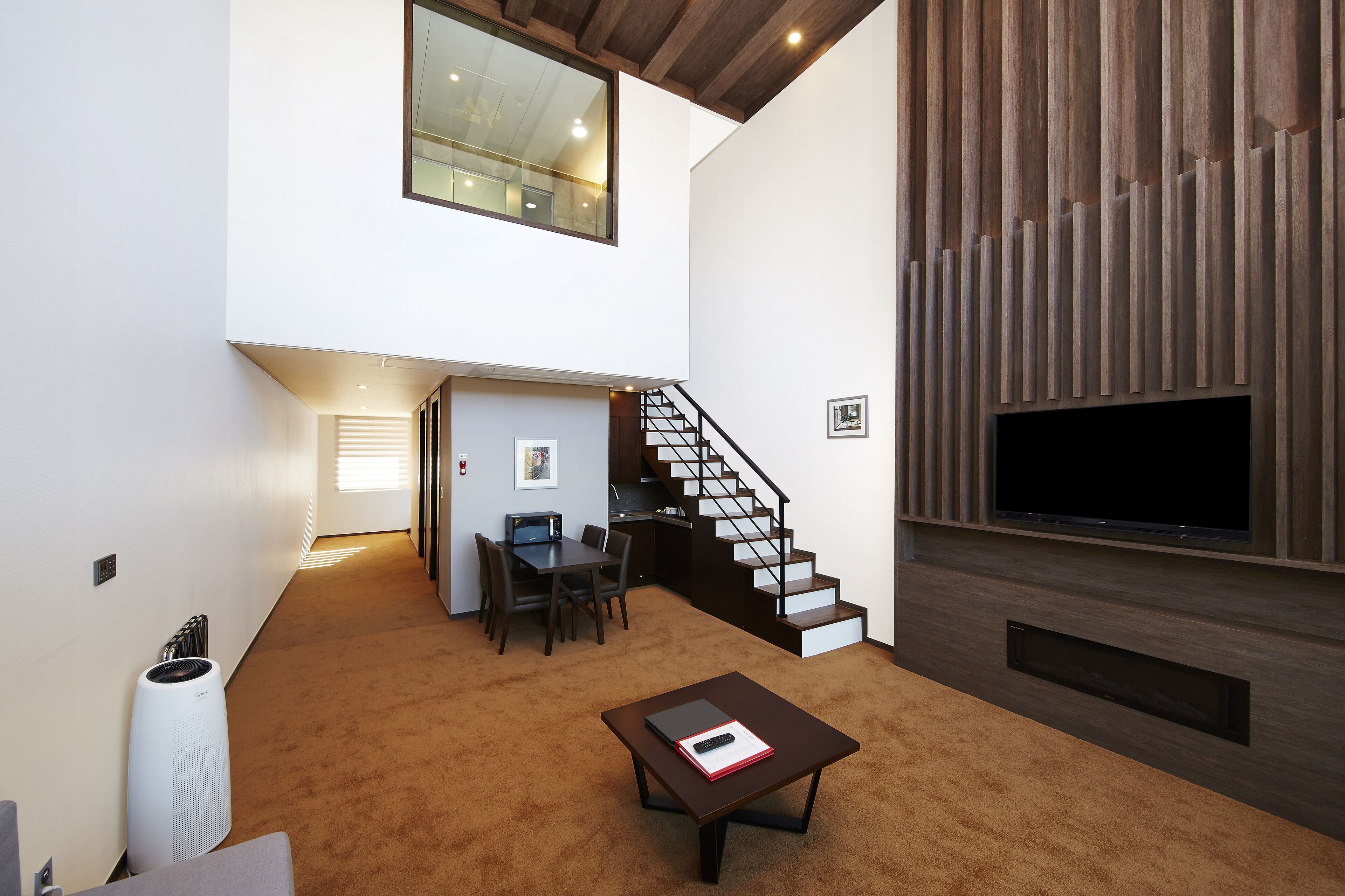 A spacious living area with a staircase, a flat-screen TV, and a dining area.