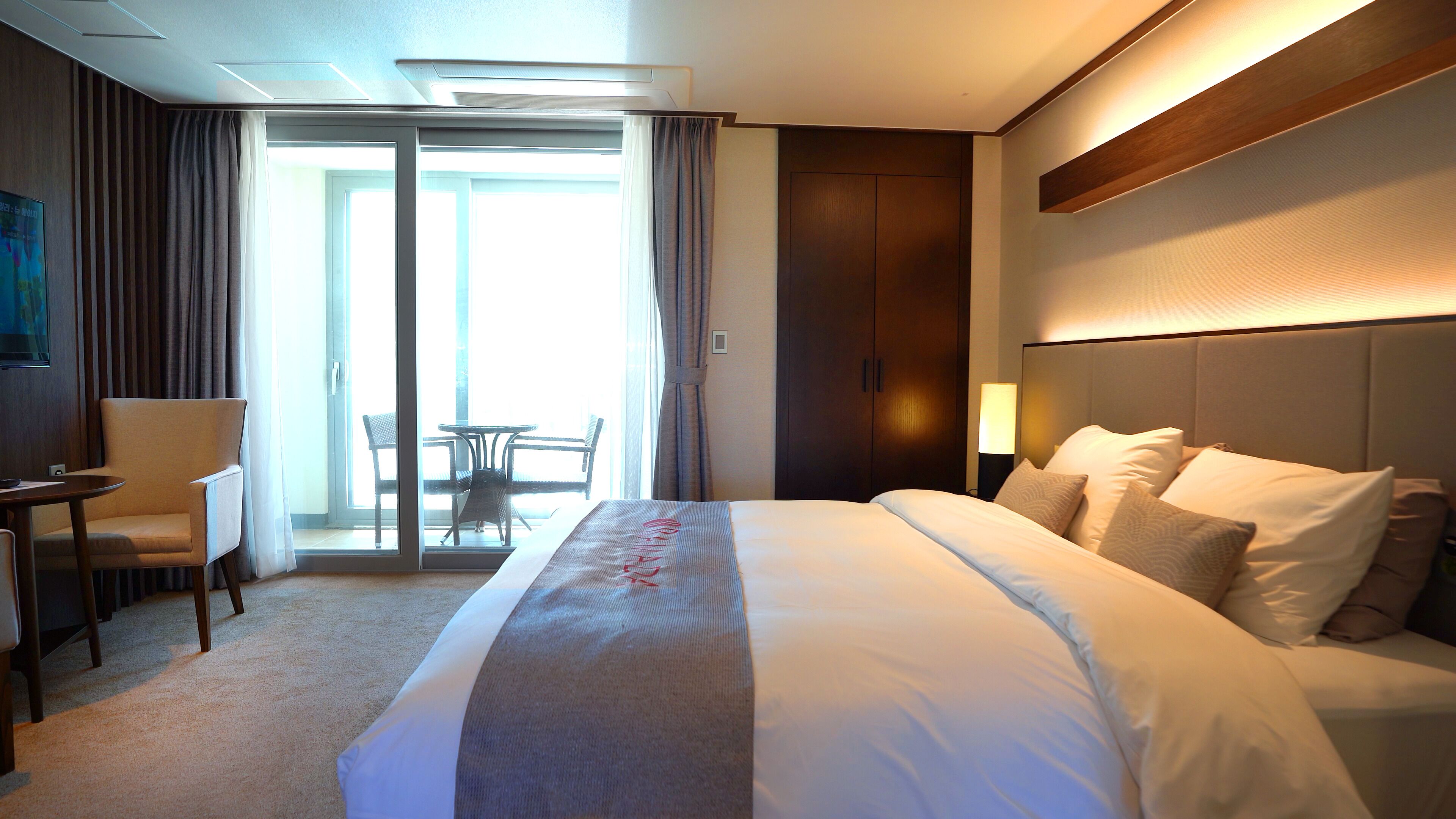 A hotel room with a large bed, a desk, a chair, and a balcony with a table and chairs.