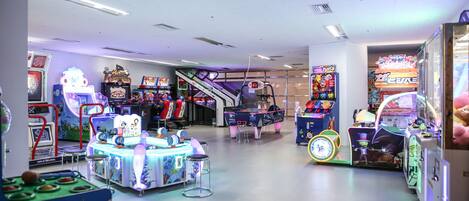An indoor arcade with various gaming machines and a central play area with stools.