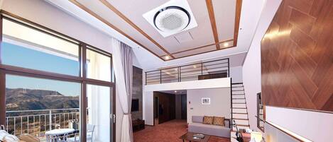 Habitación de hotel con una cama grande, una silla de masaje, un balcón con vistas a aerogeneradores y una pequeña zona de estar.