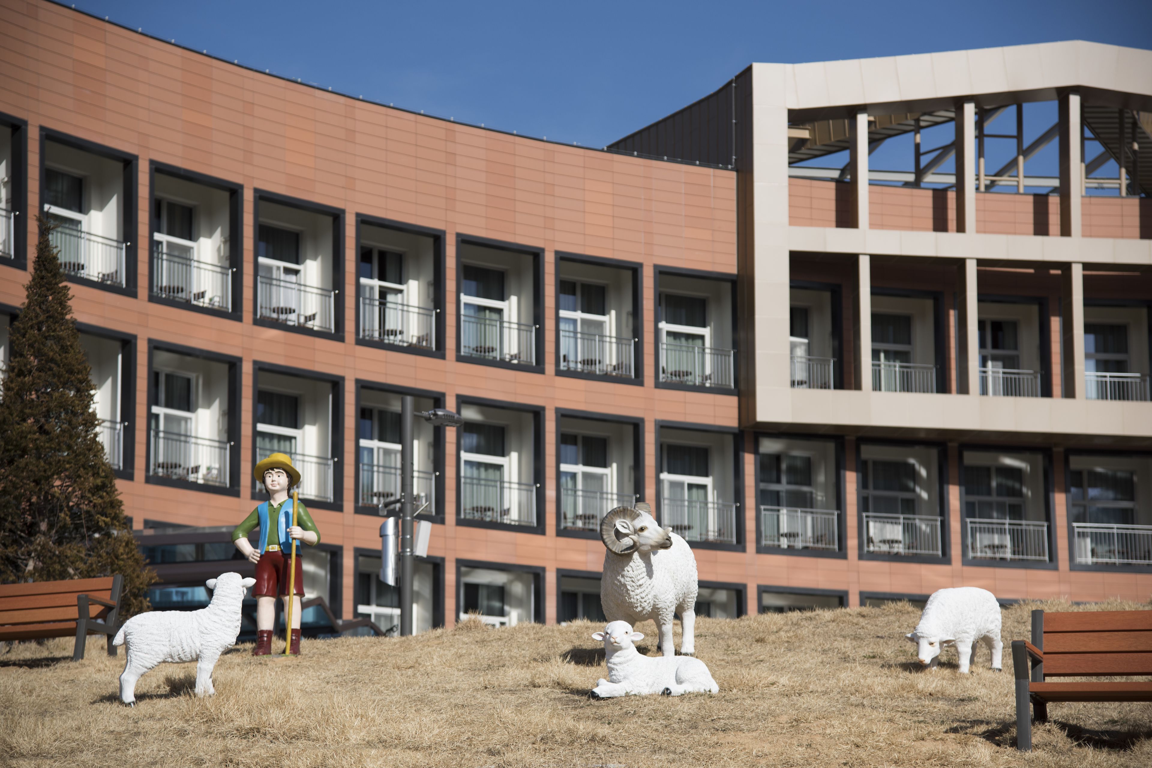 A building with multiple balconies and a grassy area with sheep sculptures.