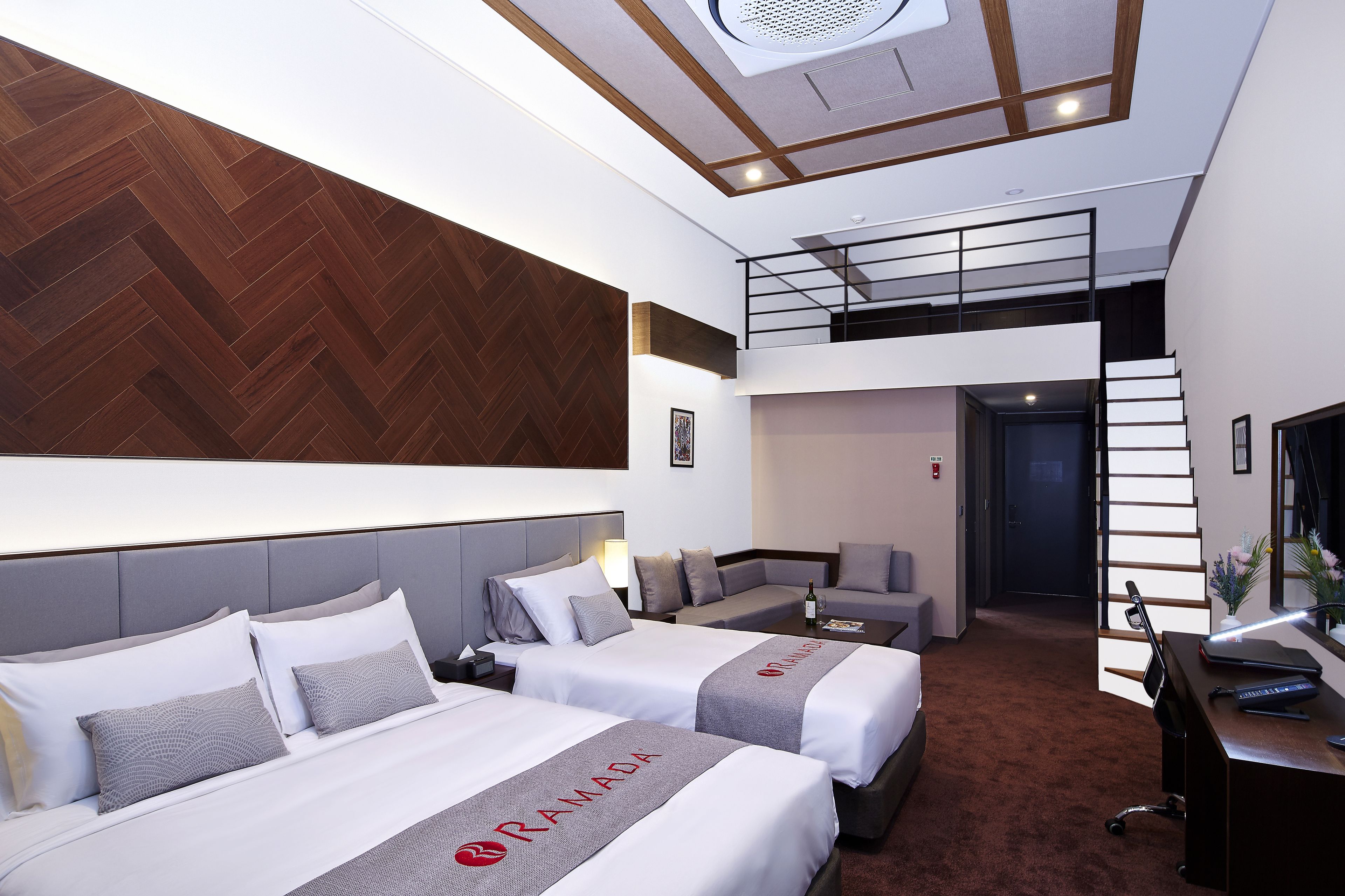 Una habitación de hotel moderna con dos camas, un sofá, un escritorio y una escalera que lleva a un nivel superior.