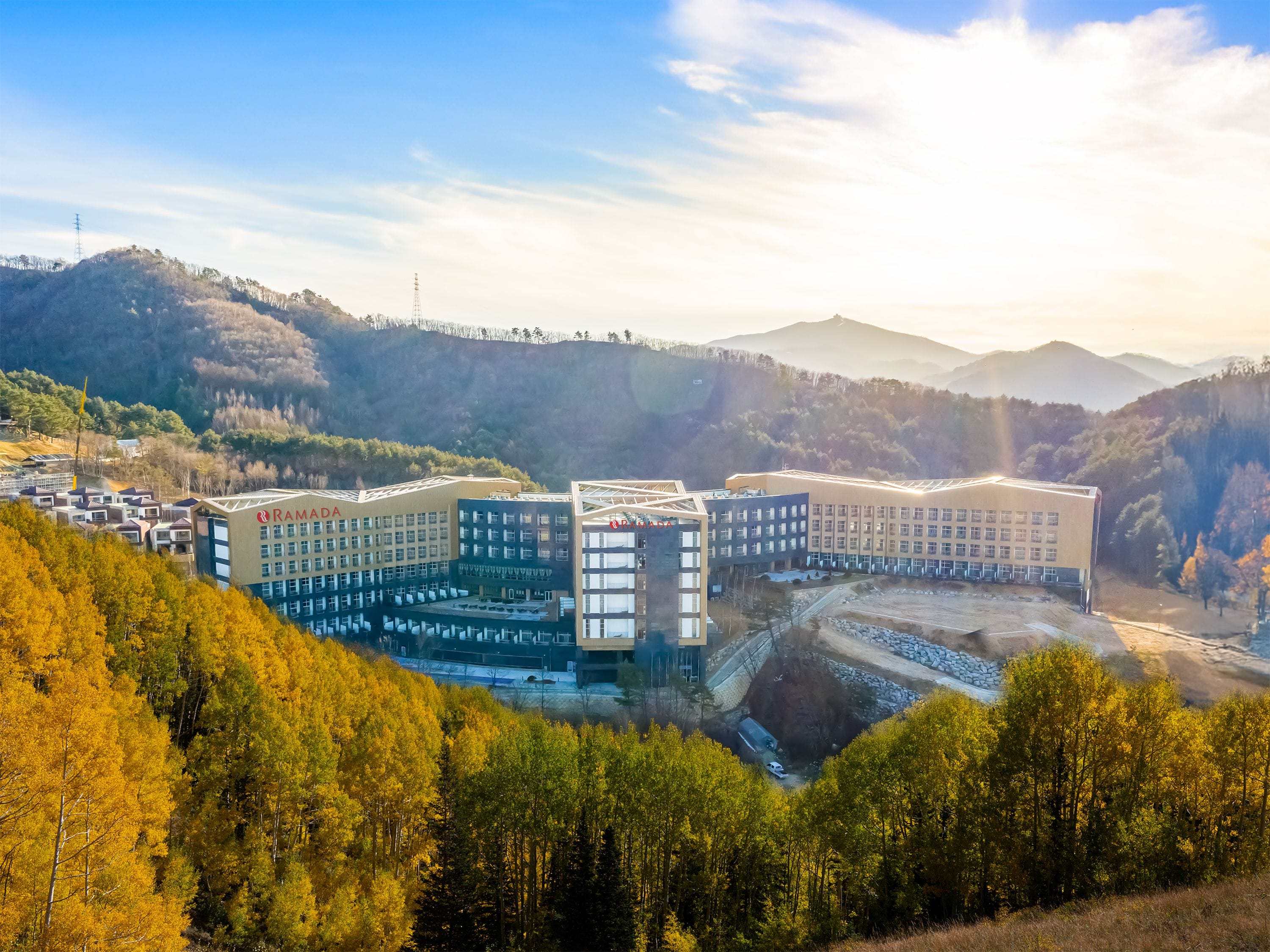 Un moderno complejo hotelero con varias edificaciones, rodeado de un paisaje boscoso y colinas.