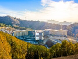 A modern hotel complex with multiple buildings, surrounded by a forested landscape and hills.