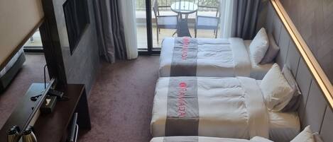 Ein Hotelzimmer mit zwei Betten, einem Schreibtisch, einem Stuhl und einem Balkon mit Tisch und Stühlen.