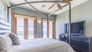Een slaapkamer met een bed, een televisie en een balkon met uitzicht op zee.