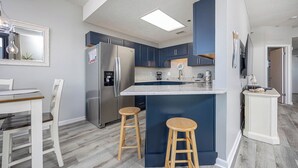 Une cuisine moderne dotée d’un îlot central, de meubles bleu foncé, d’appareils électroménagers en acier inoxydable et de tabourets en bois.