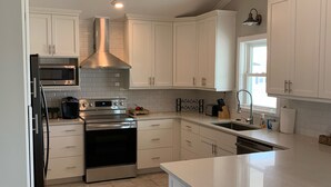 A modern kitchen with white cabinetry, stainless steel appliances, and a large island with bar stools. - Canal/w dock, pool, ocean view, 1 block from beach & EV charger (Ocean Isle Beach)