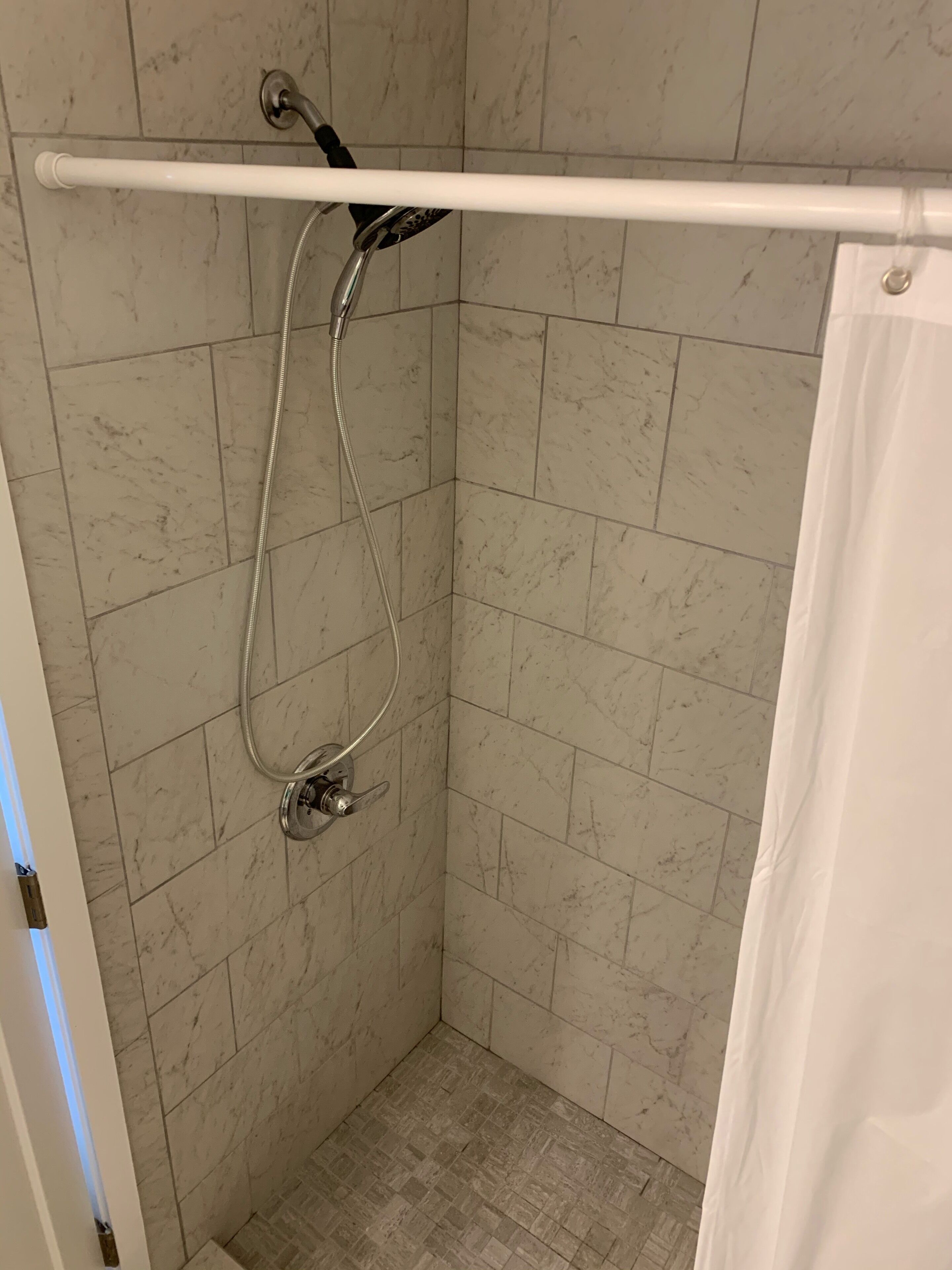 Un área de ducha pequeña con azulejos, una barra de apoyo y un cabezal de ducha.