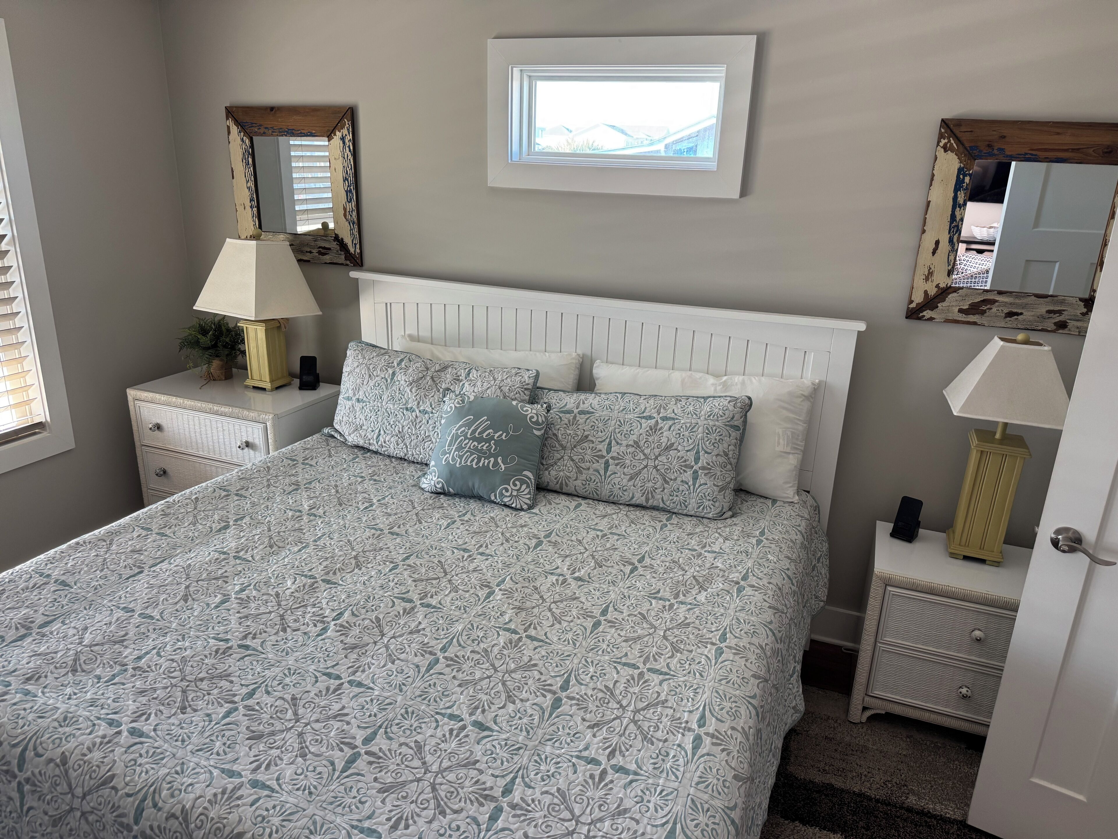A bedroom with a bed, two nightstands, a lamp, a mirror, and a window.