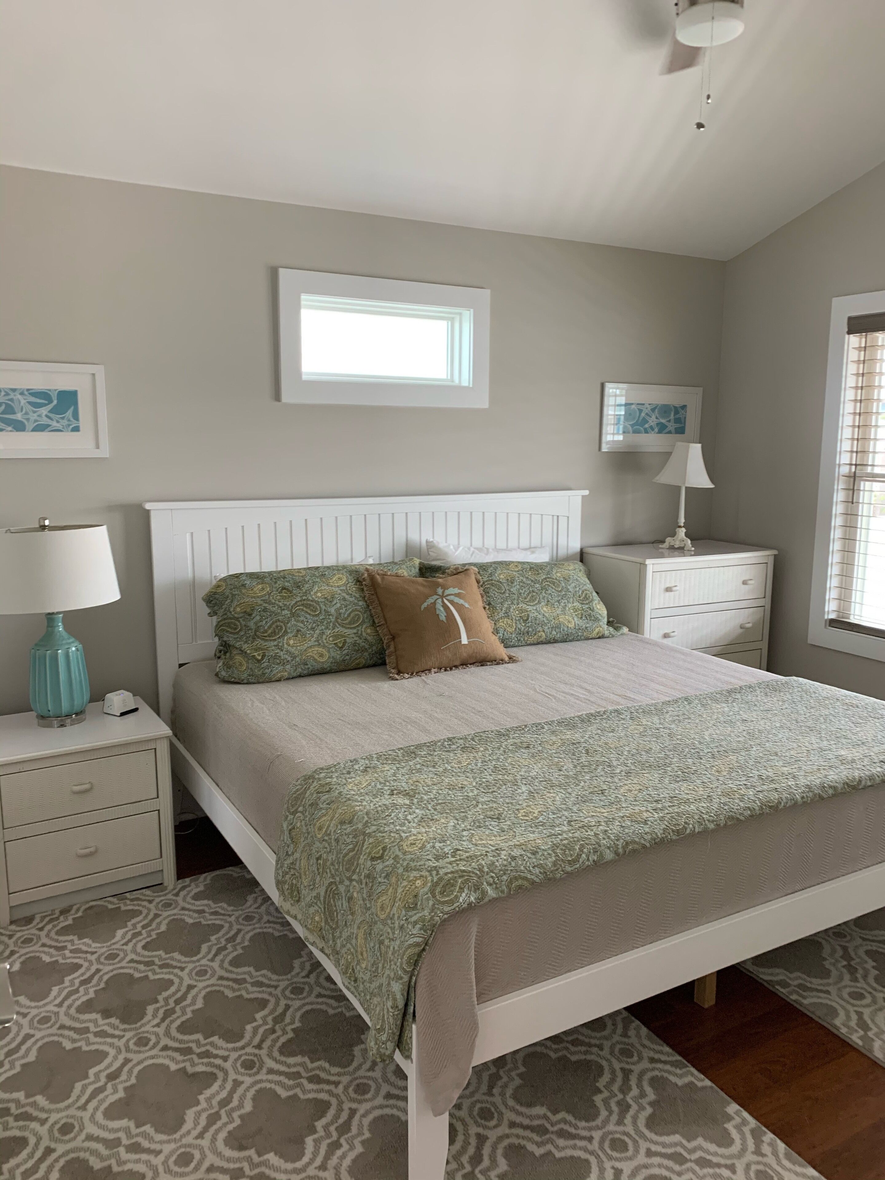 Quarto com cama, mesas de cabeceira, janela e ventilador de teto.