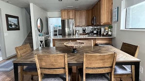 Une cuisine moderne avec des meubles en bois, un réfrigérateur en acier inoxydable et un coin repas comprenant une table et des chaises en bois.
