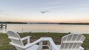 Two white Adirondack chairs facing a calm lake at sunset with a dock and greenery in the background. - Cozy Cottage Goodland Fl.  (GOODLAND)