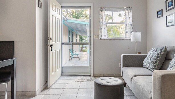 A living room with a sofa, ottoman, and a view through a door to an outdoor patio. - Cozy Cottage Goodland Fl.  (GOODLAND)