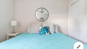 A bedroom with a bed, a round mirror, a ceiling fan, a nightstand with a lamp, and a door. - Cozy Cottage Goodland Fl.  (GOODLAND)