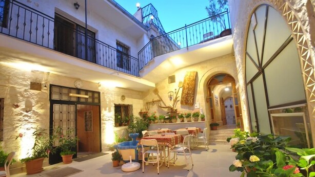 Un patio con mesas al aire libre, plantas en macetas y una escalera que lleva a un nivel superior.