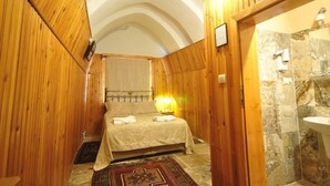 Un dormitorio acogedor con techo de madera, una cama con colcha estampada y zona de ducha con suelo de piedra.