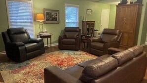 Un salon avec un canapé en cuir marron, deux fauteuils, une table basse et un tapis à motifs.
