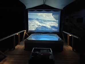 Una vasca idromassaggio con uno schermo che mostra un paesaggio innevato, circondata da pavimento e ringhiere in legno.