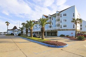 A multi-story hotel with a parking lot, palm trees, and a clear sky.