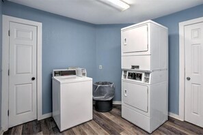 A laundry room with two stacked washers and dryers, a trash can, and white doors.