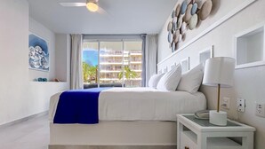 A bedroom with a bed, a nightstand, a ceiling fan, a window with curtains, and a wall with decorative plates.