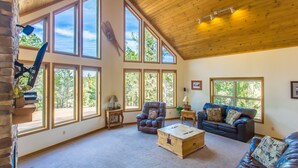 A spacious living room with large windows, a wooden ceiling, and a cozy fireplace.