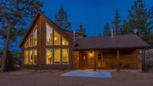 A wooden cabin with large windows, a porch with seating, and a satellite dish.