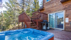 A wooden deck with a hot tub, a barbecue grill, and a staircase leading to a deck area.