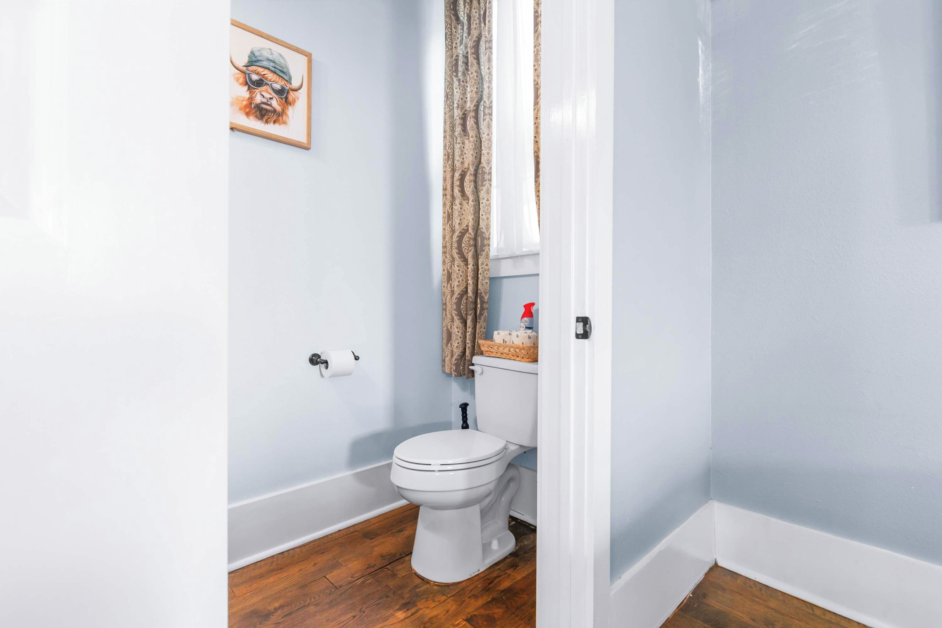 Een badkamer met een wit toilet, houten vloeren, een toiletrol en een decoratief object aan de muur.