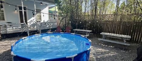 Una piscina fuori terra blu con un cartello di sicurezza, circondata da un pontile in legno e una staccionata di bambù.