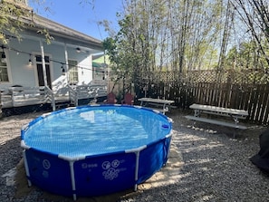 A blue above-ground pool with a safety sign, surrounded by a wooden deck and a bamboo fence.