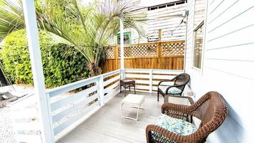 A covered patio with wicker furniture, a wooden fence, and lush greenery.