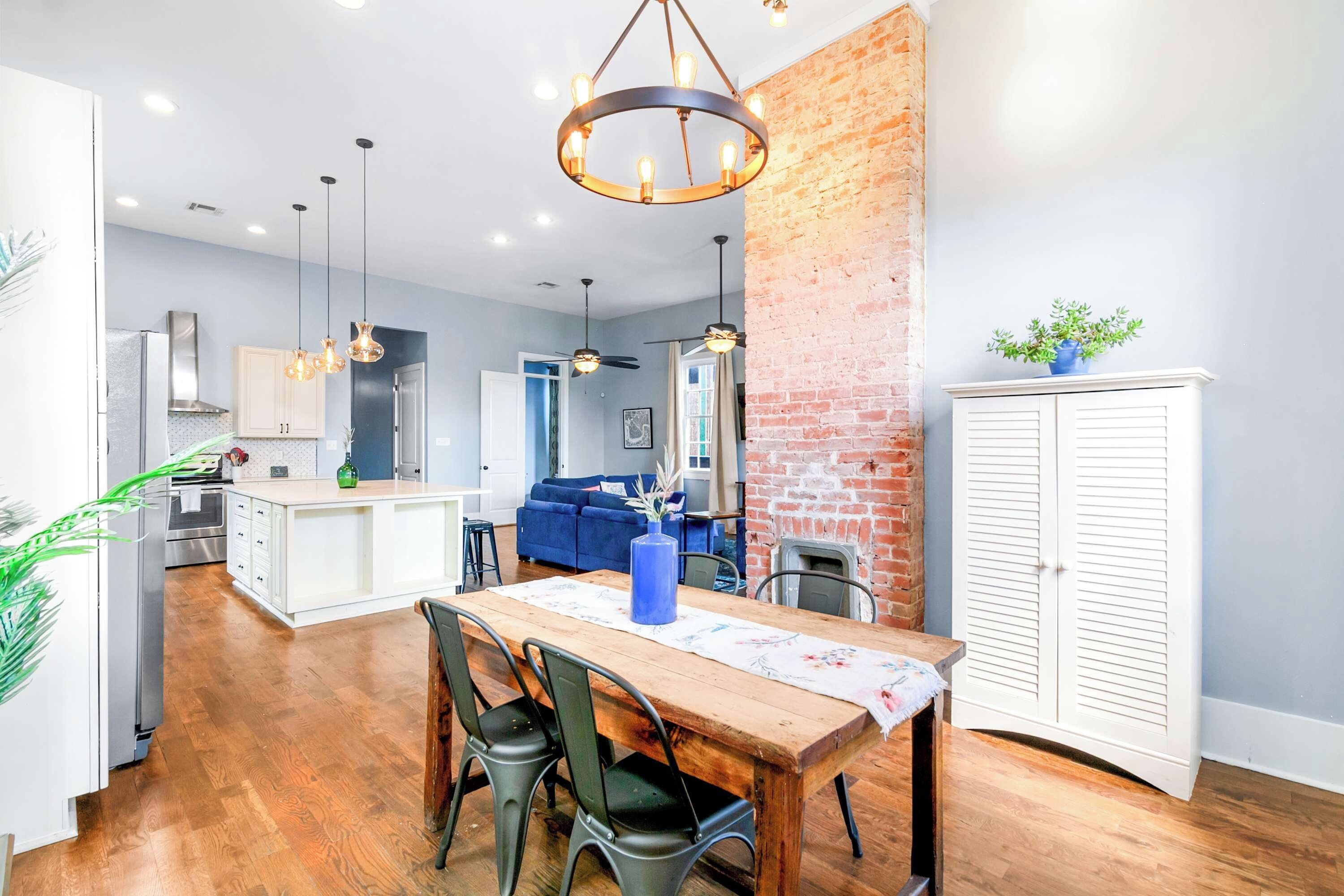 A modern kitchen with a central island, a dining area with a wooden table and chairs, and a living space with a blue sofa.
