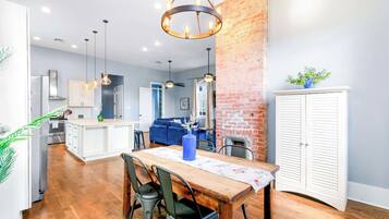 A modern kitchen with a central island, a dining area with a wooden table and chairs, and a living space with a blue sofa.