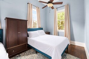 Une chambre à coucher comprenant un lit, une armoire, un ventilateur de plafond et deux fenêtres avec des rideaux.