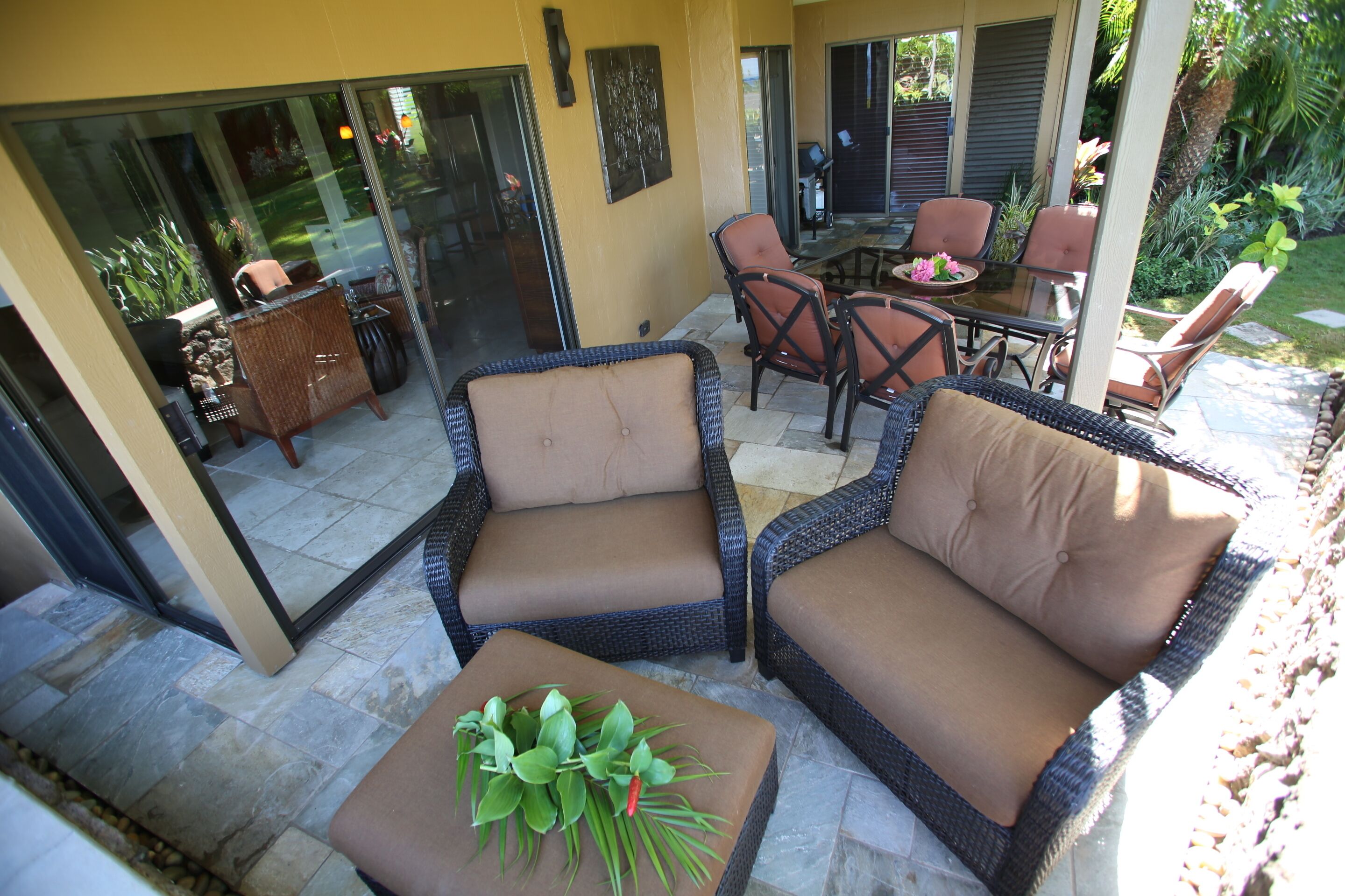 Un patio con mobiliario de mimbre, incluyendo dos sillones y una mesa, además de una pequeña mesa con una planta.
