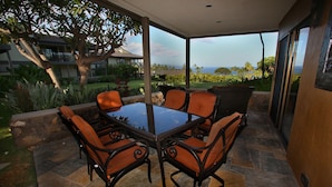An outdoor patio with a glass-top table and chairs, surrounded by stone flooring and a view of a residential area and the ocean. - Wailea Elua #207 Ocean and Garden View Short Walk to the BEACH ..Not 14 Min (Wailea)