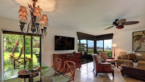 A spacious living area with a glass dining table, wicker chairs, a sofa, and a television. - Wailea Elua #207 Ocean and Garden View Short Walk to the BEACH ..Not 14 Min (Wailea)