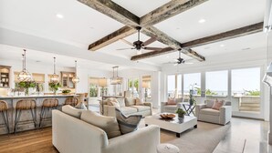 A spacious living area with a high ceiling, exposed beams, and large windows offering a view of the outdoors. - Stay @ Sea Star on Isle of Palms (Isle of Palms)