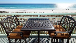 Une table et des chaises sur un balcon donnant sur une plage, avec une clôture et une jetée en arrière-plan.