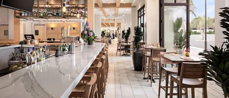 Uma área de bar moderna com bancada de mármore, banquetas de madeira e uma variedade de garrafas e copos.