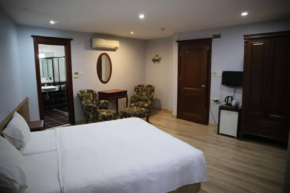 A hotel room with a bed, two chairs, a small table, a mirror, a TV, and a wardrobe.