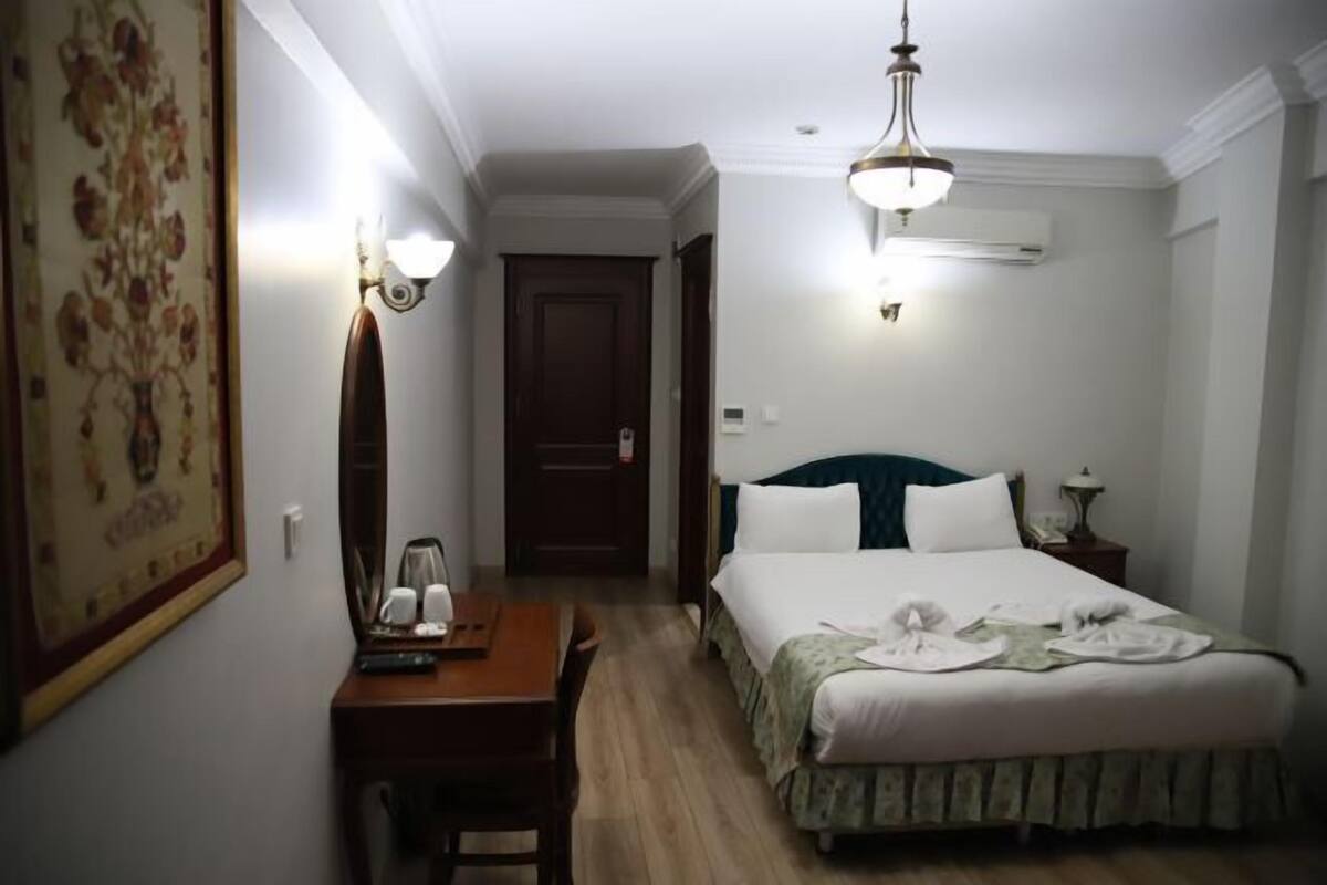 A hotel room with a bed, bedside table, lamp, and a door.