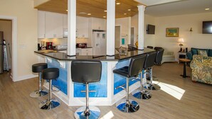 A modern kitchen with white cabinets, a central island with bar stools, and a wooden ceiling. - "Sandy Dunes" - Oceanfront Home w/ Private Pool, 8 Bedrooms / 6.5 Bathrooms (Holden Beach)
