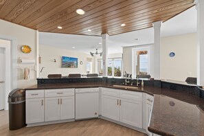 A spacious kitchen with a large island, white cabinetry, and a wooden ceiling.