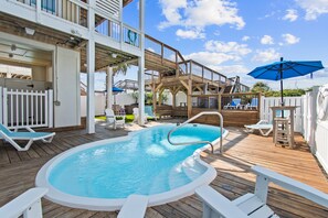 A pool area with a hot tub, lounge chairs, and a wooden deck.