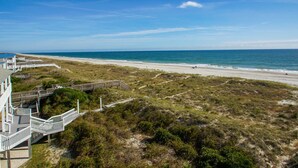 A coastal view with a beach, a wooden boardwalk, and a building with a white facade and balconies. - "Sandy Dunes" - Oceanfront Home w/ Private Pool, 8 Bedrooms / 6.5 Bathrooms (Holden Beach)
