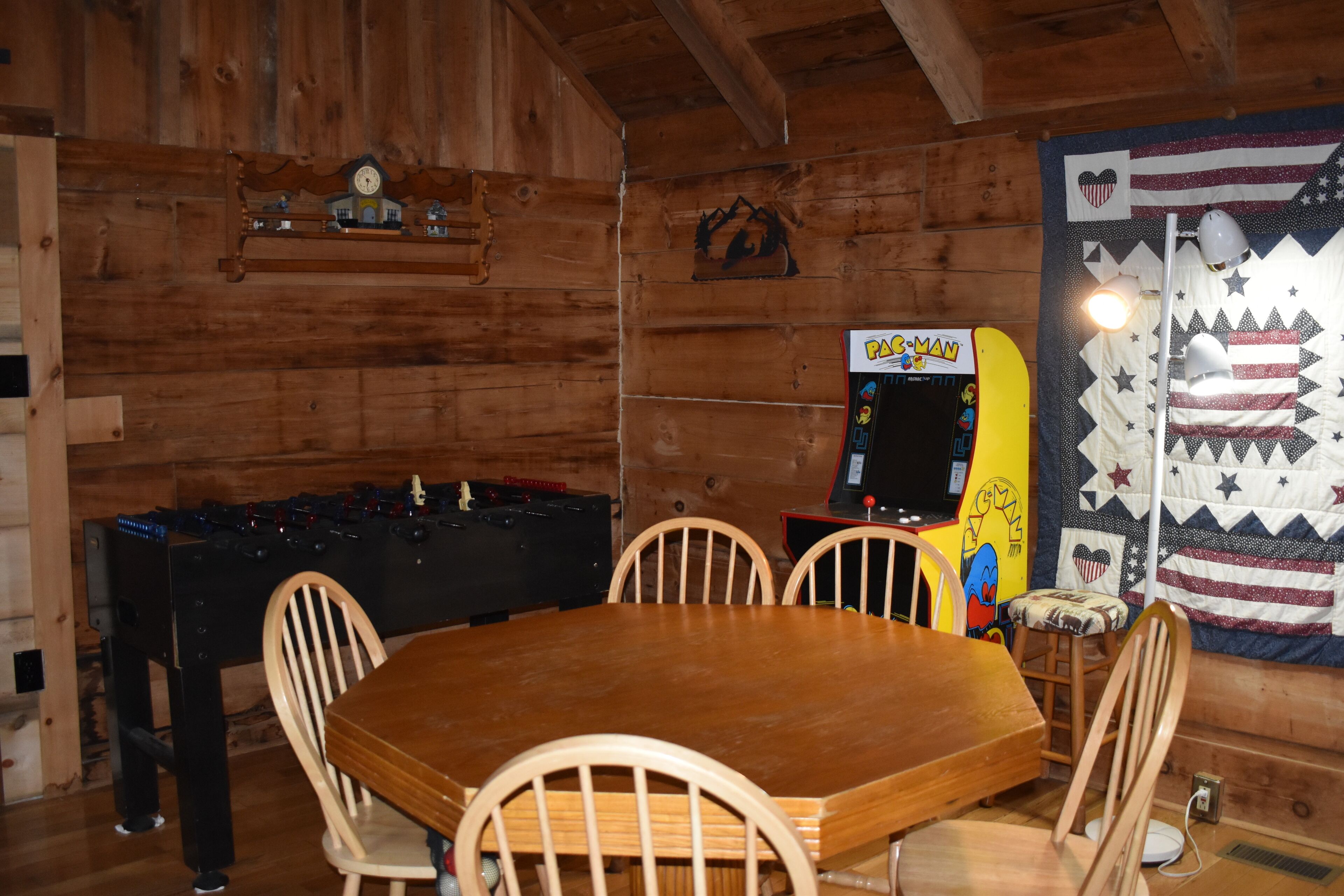 Een houten interieur met een tafelvoetbaltafel, een tafel met stoelen en een quilt met een Amerikaans vlagdesign.