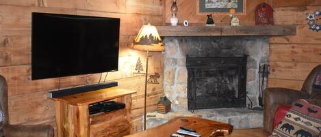 Een houten blokhut interieur met een stenen open haard, houten meubels, een bevestigde televisie en een gezellige zithoek.